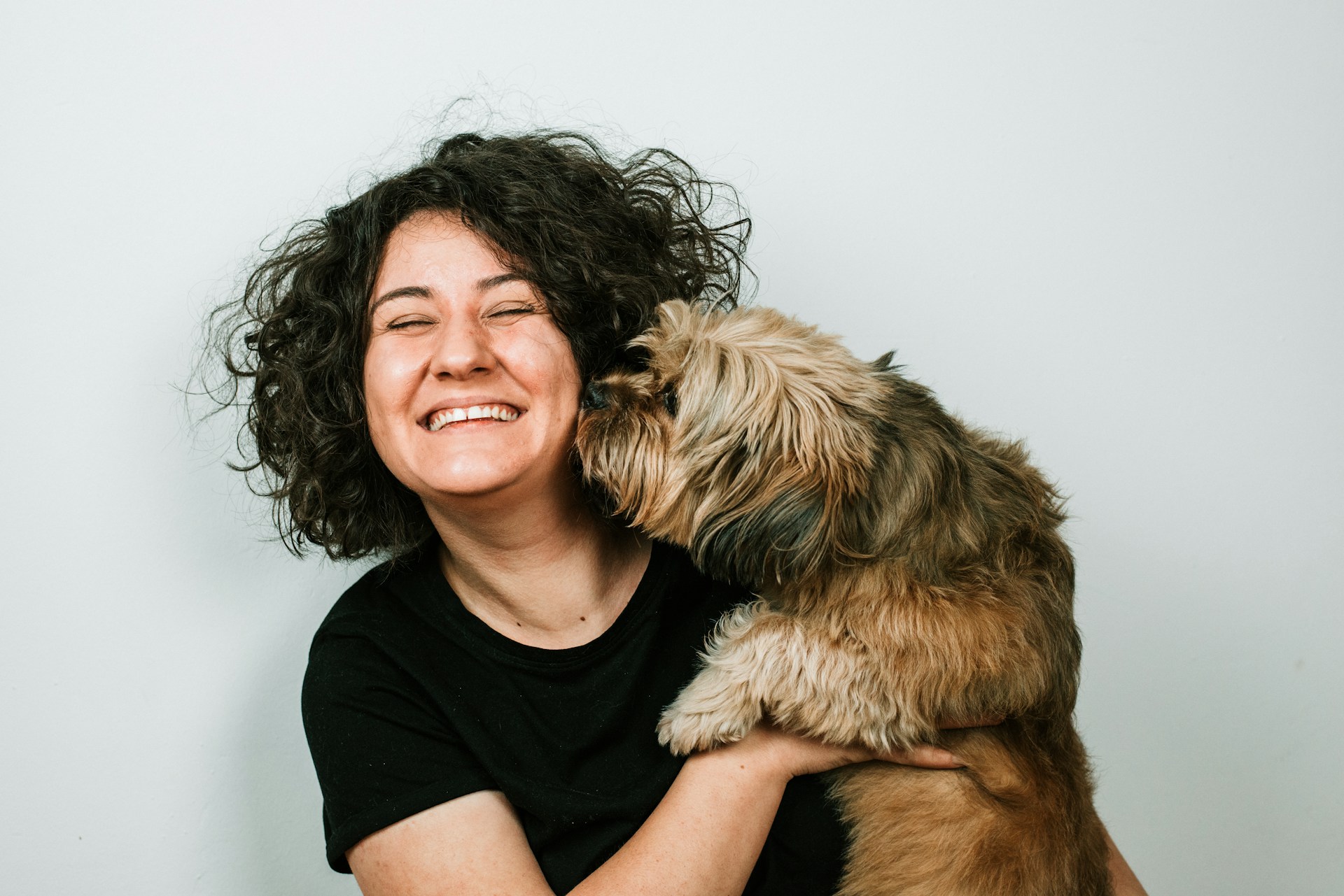 woman smiling as small brown dog licks her cheek